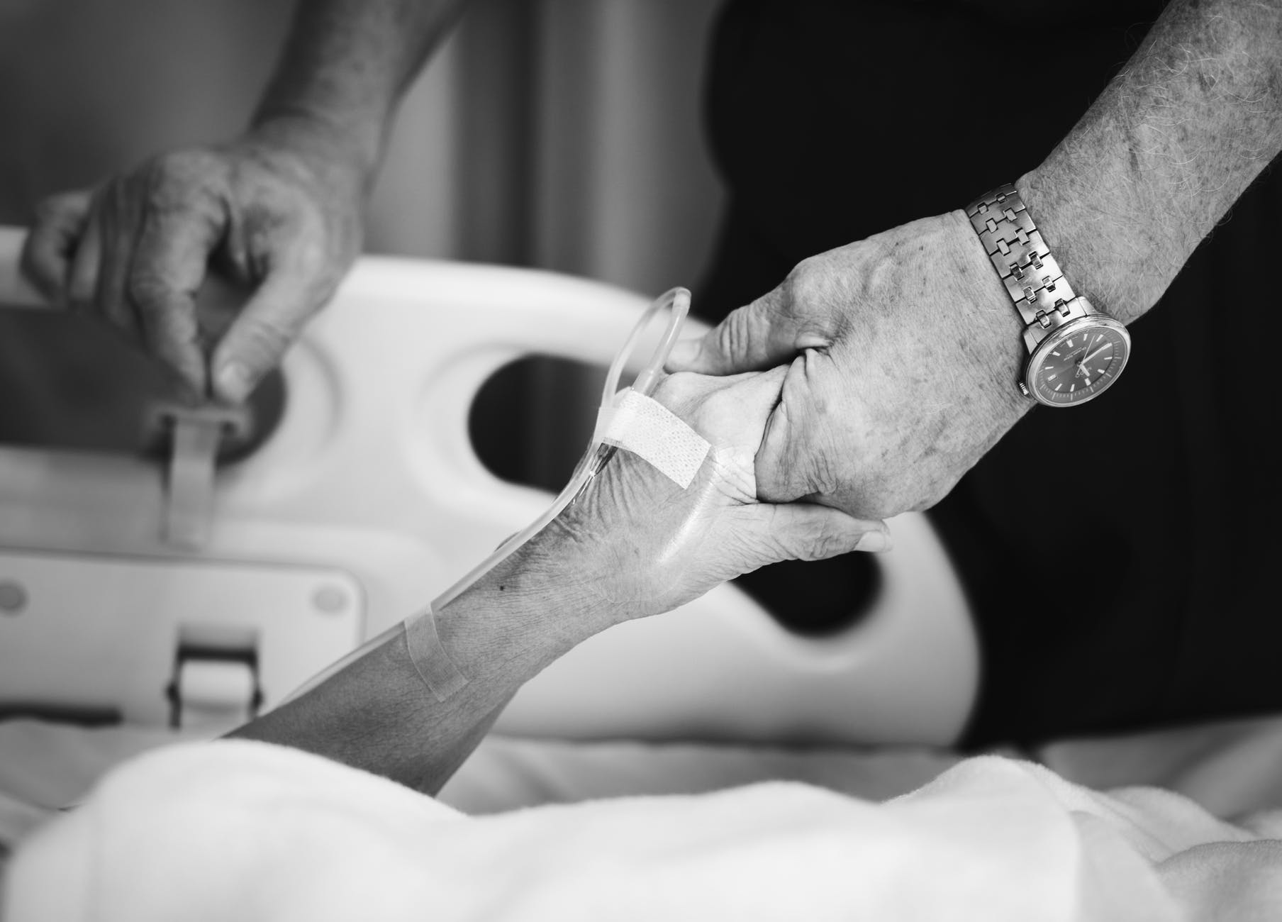 grayscale photography of patient and relative holding hands
